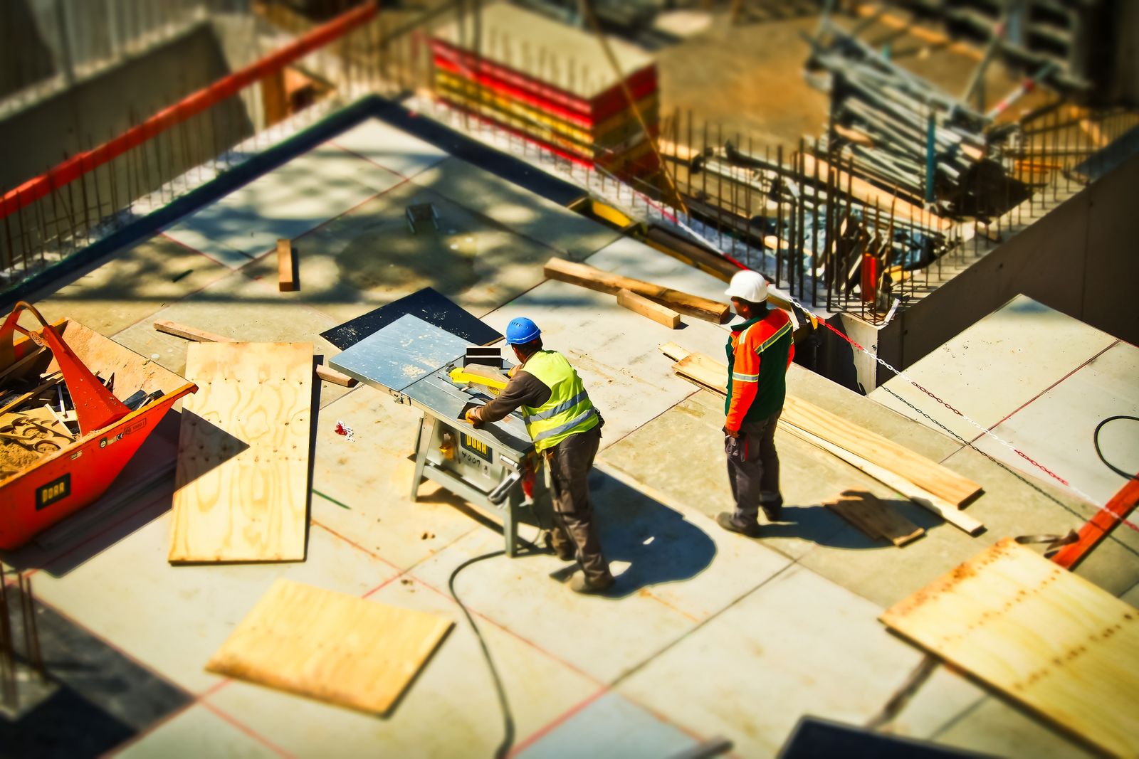 Two builders in hi-vis working with timber and a bench saw on a construction site