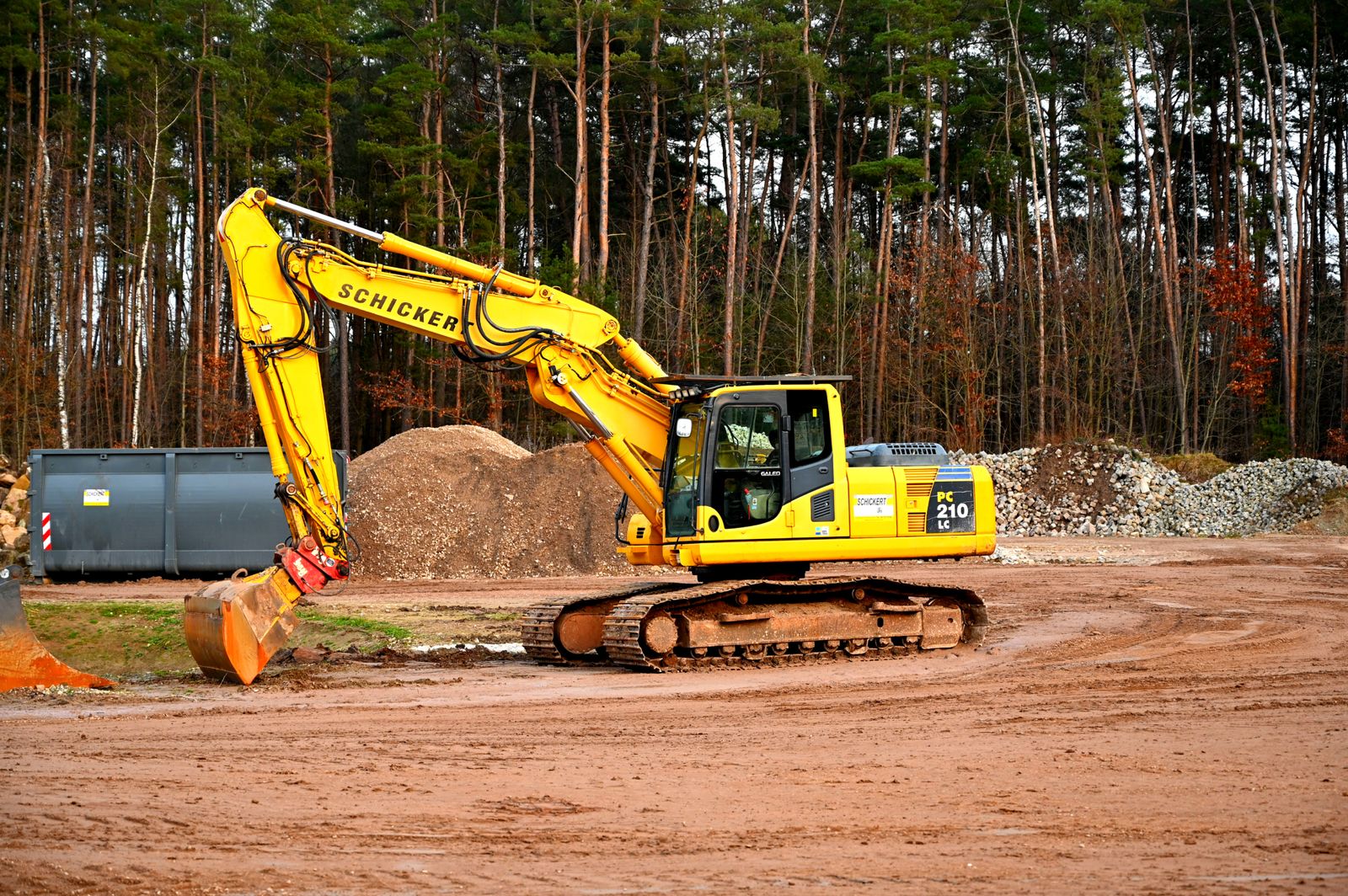Yellow tracked excavator on a groundworks site with soil and aggregate stockpiles
